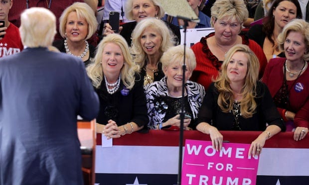 Several platinum-blond white women stare intently at Donald Trump as he speaks to them at a campaign rally in 2016. Their expressions are rapturous, mouths open and eyes wide, and one women even appears to be licking her lips.