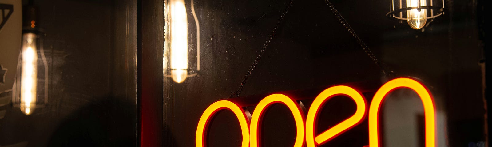 A yellow sign that says OPEN, against a dark background with some lightbulbs