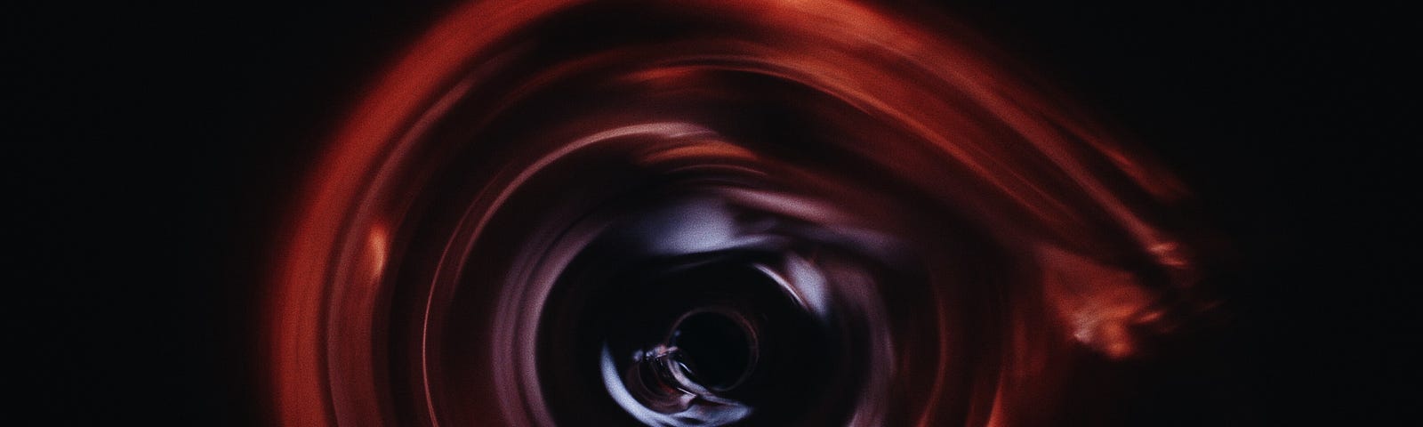 A red circle or spiral on a black background. Depicts a black hole.