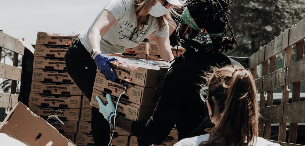 Volunteers move boxes off a truck with their masks on.