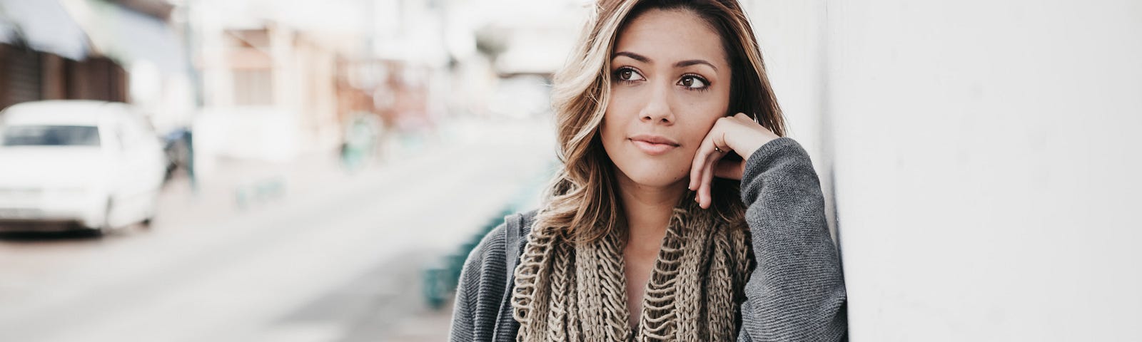 A woman wearing a scarf pauses on a street to think.