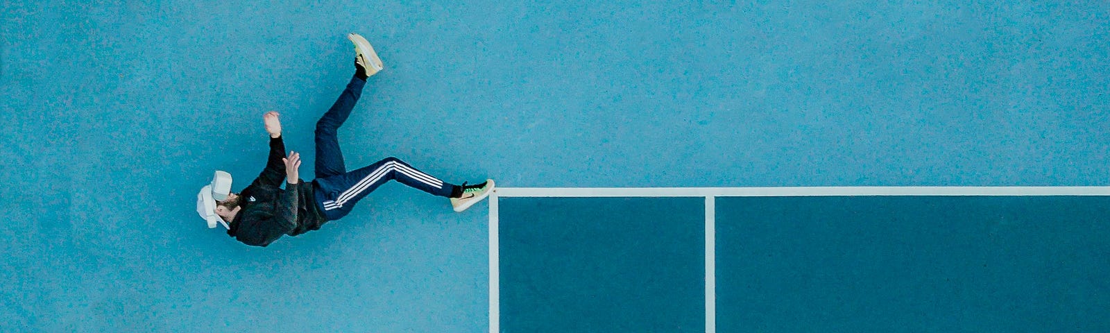 An illusion of a person falling as they lie on their side at the edge of a tennis court.