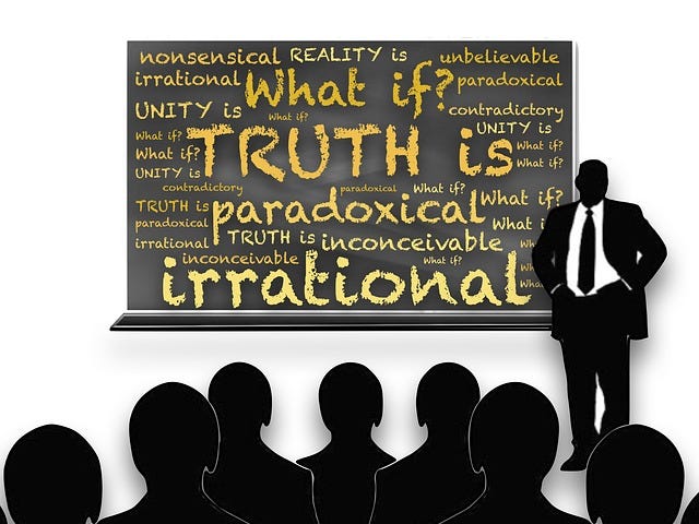An image of teacher standing in front of a blackboard that says “What if” and “ Truth is paradoxical , irrnational.”
