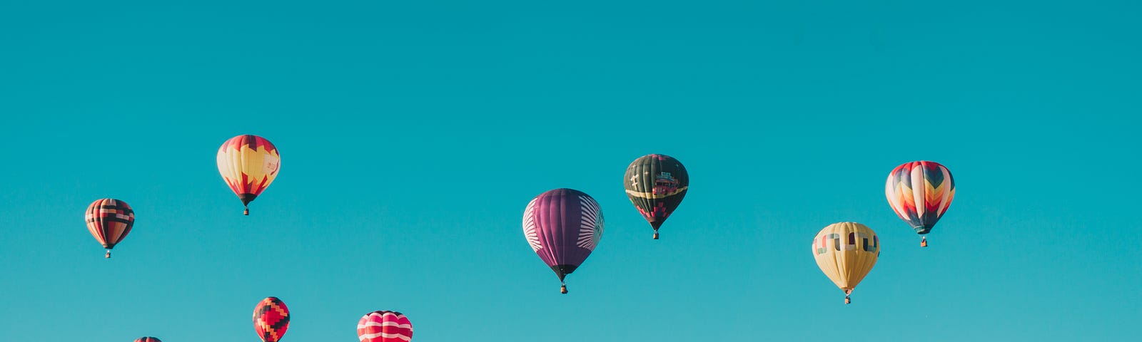 Dozens of colourful hot air balloons in a clear blue sky.