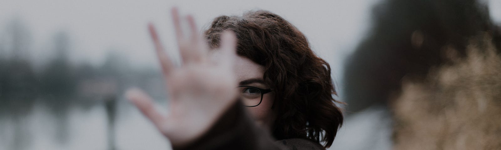 Woman with glasses putting hand up with her palm towards the camera.