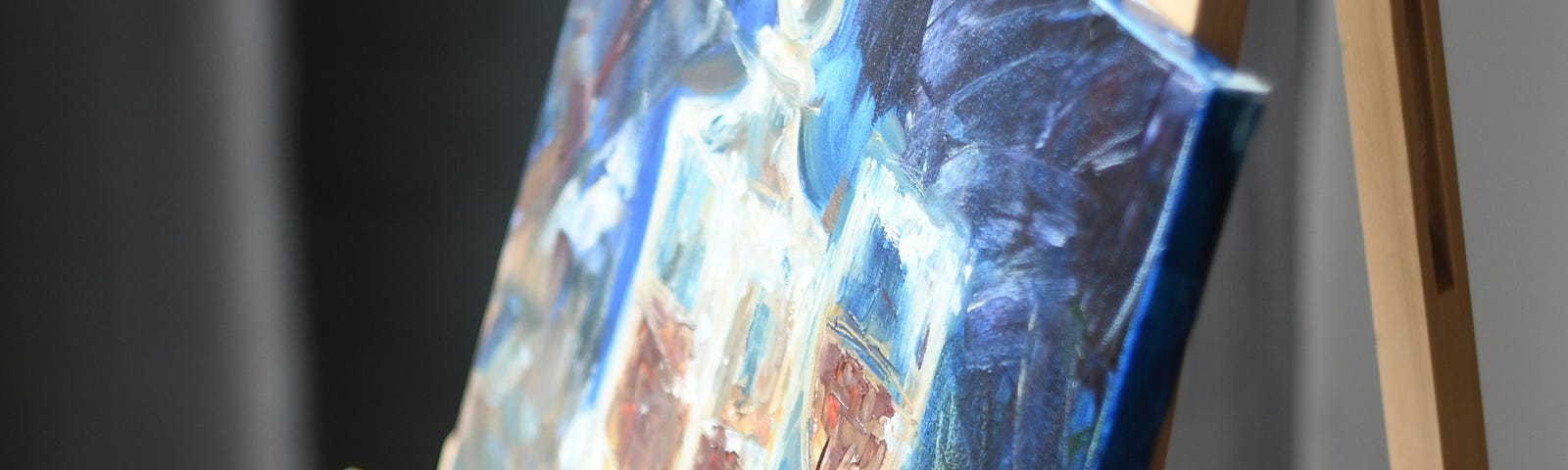 a painting on an easel- there are dark blues, whites, surrounding a glass and carafe