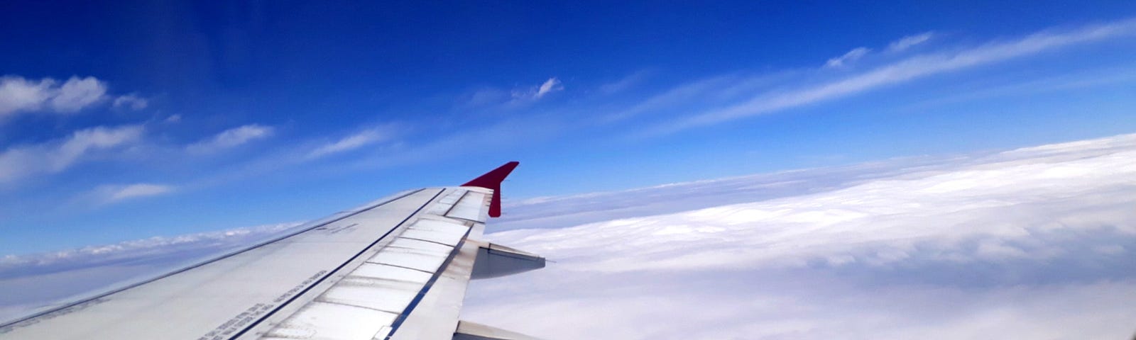 Image through an airplane window showing wing of plane above clouds