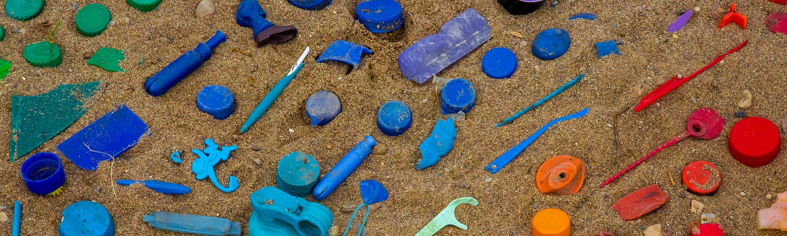 Plastic waste arranged by colours on a sandy beach