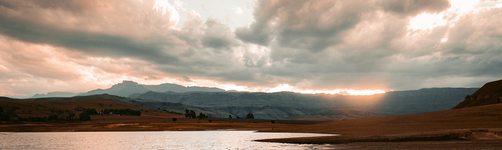 Parched ground with receding water, mountains and sunrise (set) in the background