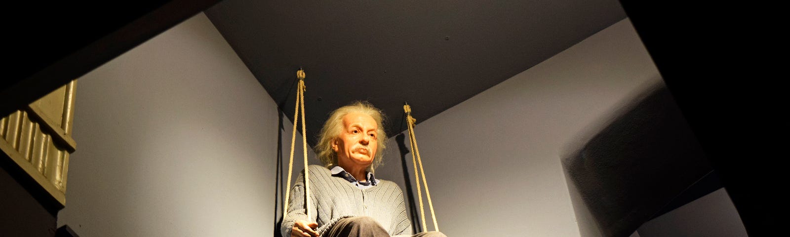 Einstein is shown in this image as a doll, hanging off the ceiling on a swing. Theory of everything.