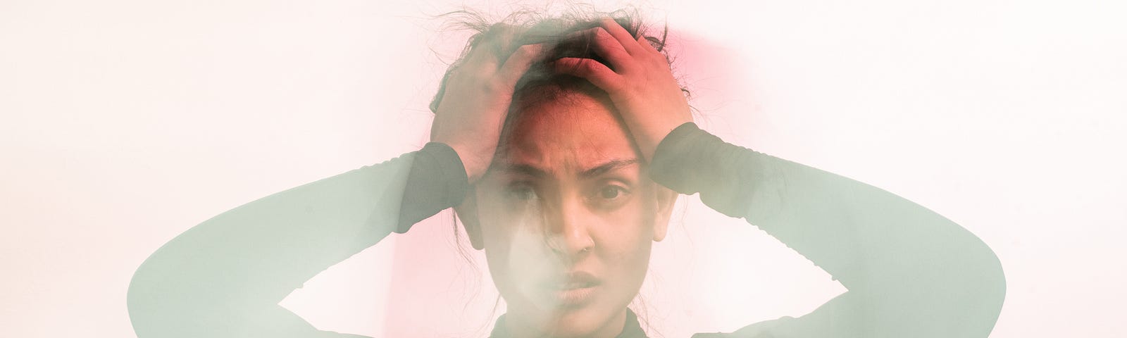 A woman in a green sweater holding her head. There is a small layer of fog or blurring over the picture.