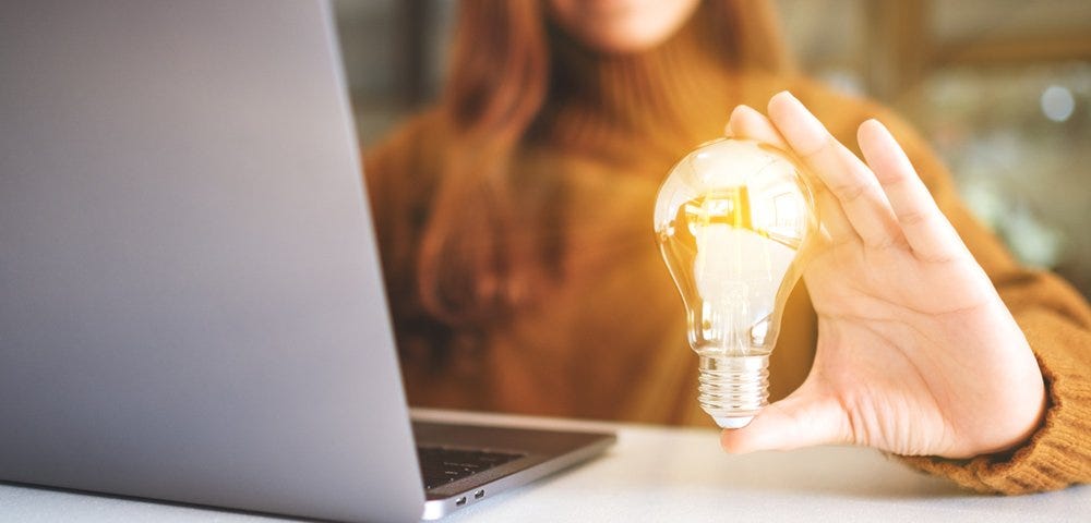 Woman holding a shining light bulb next to a laptop
