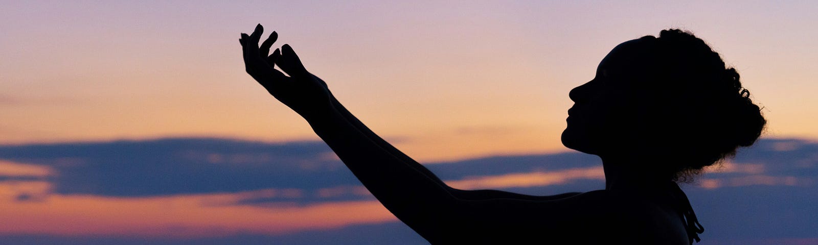 Silhouette of a woman standing by the ocean with sunset in the background.