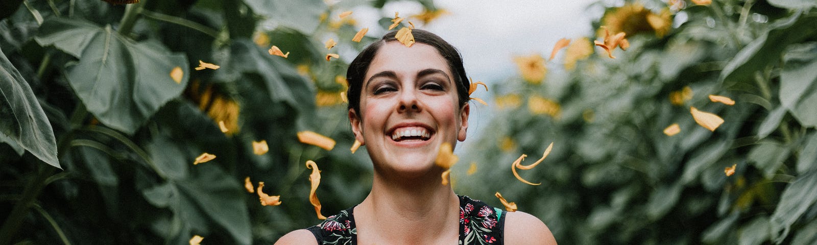 Image of woman laughing surrounded by plants and petals.