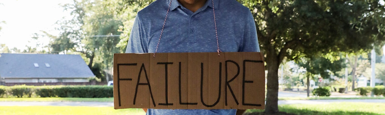 A man with a cardboard sign necklace that reads “failure.”