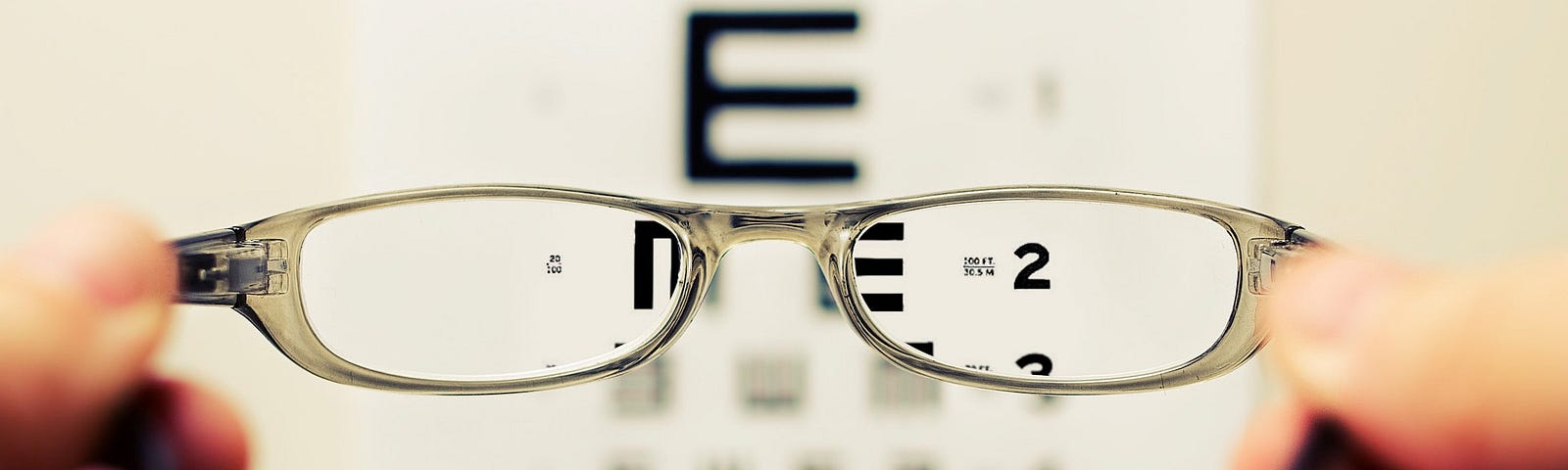 Hands hold up a pair of glasses in front of an eye chart, clarifying blurry letters