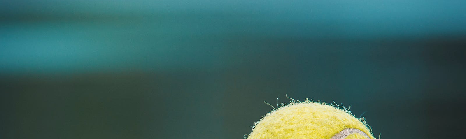 A close-up of a tennis ball landed on the corner intersection of the lines of a court. The court is glassy like a mirror and the clear reflection of the ball on the line is visible.