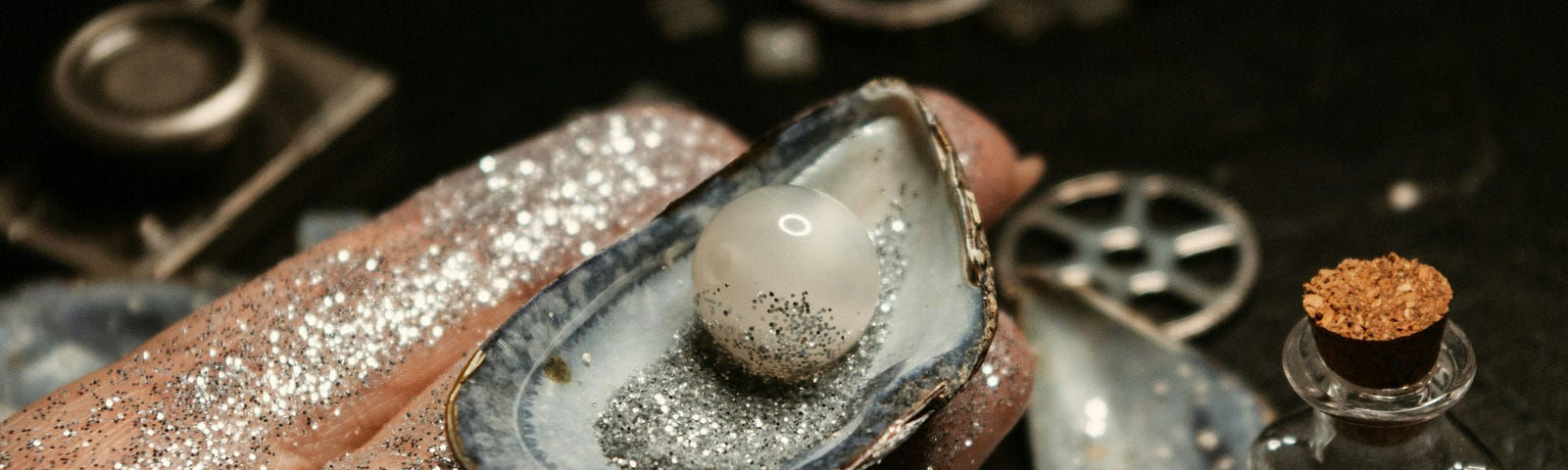 Pearl in a shell on a hand dusted with glitter.