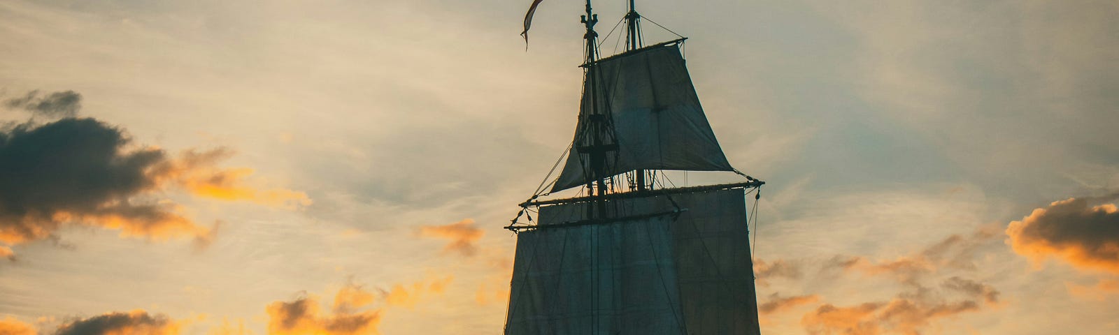 A pirate ship sailing to the horizon with the bright orange sunset unfolding before it.