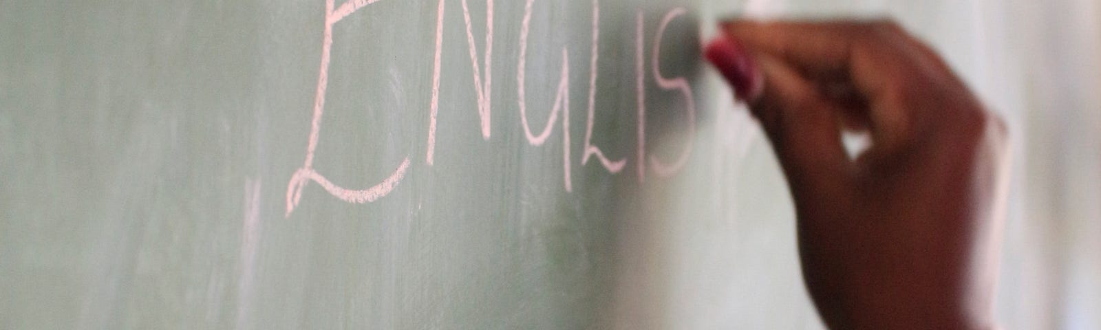 Hand holding a chalk, writing English on the chalkboard.