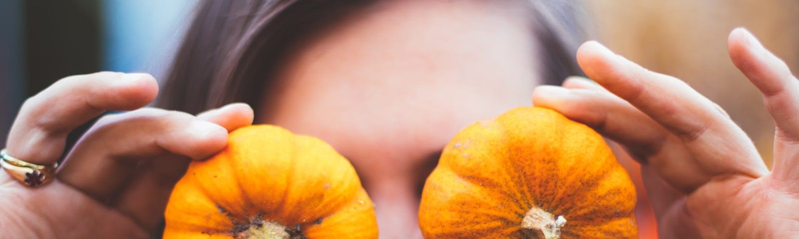 Smiling woman holding two small pumpkins in front of her eyes.