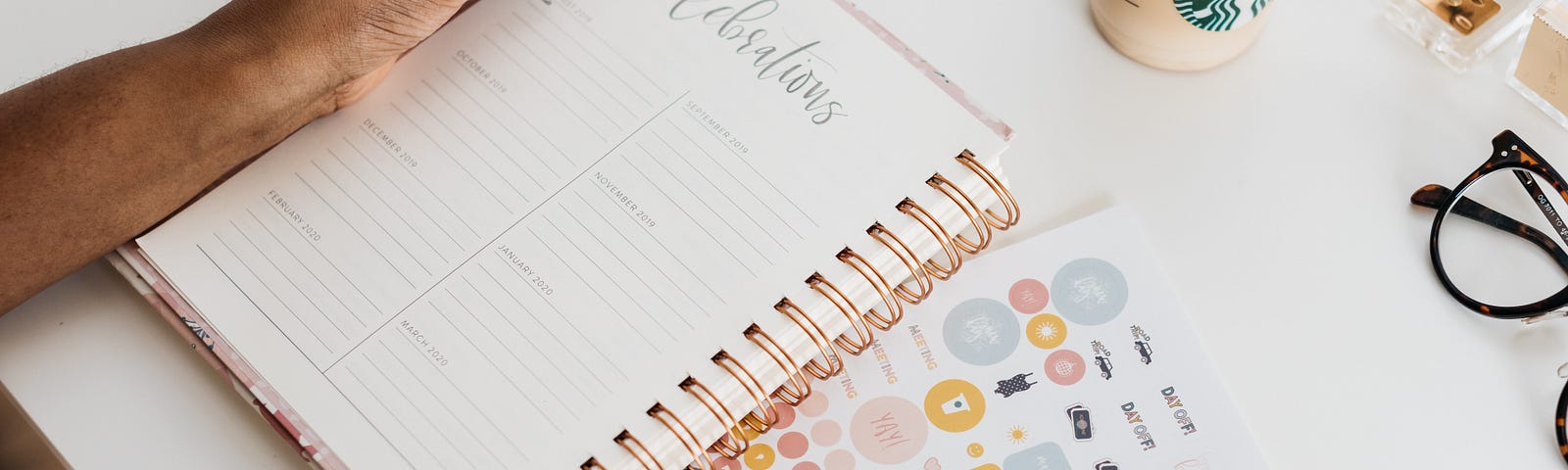 Black person writing in a planner with cup of coffee on desk and stickers