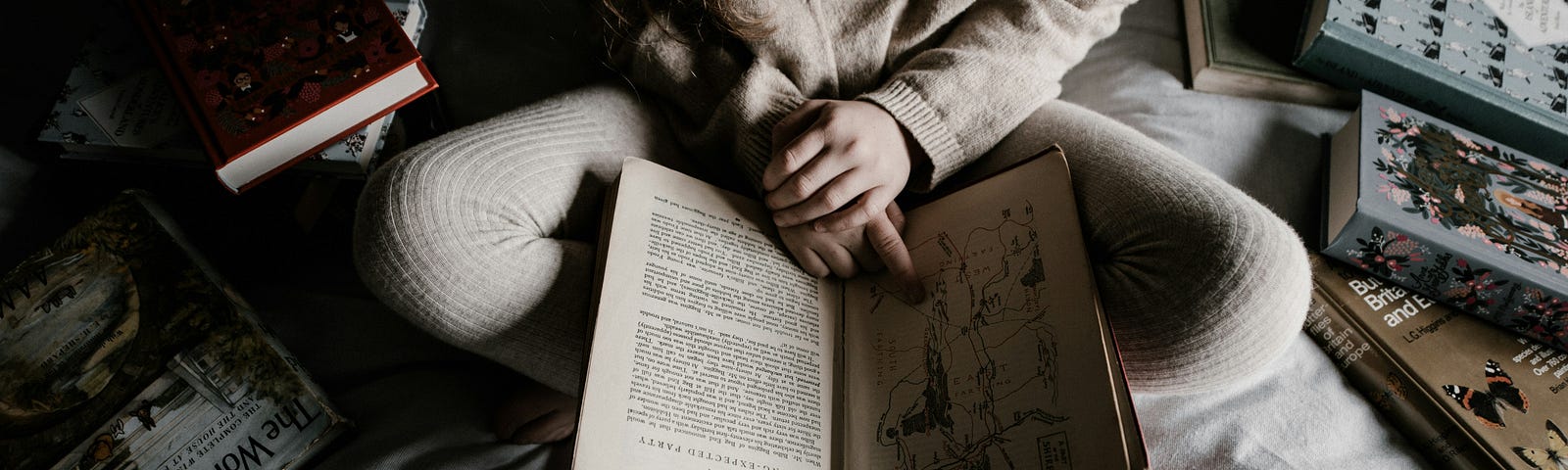 A person sitting cross-legged on a bed, surrounded by books, deeply engrossed in reading. The warm, muted tones of the scene create a calming and introspective atmosphere, perfectly capturing the quiet moments of reflection before sleep.