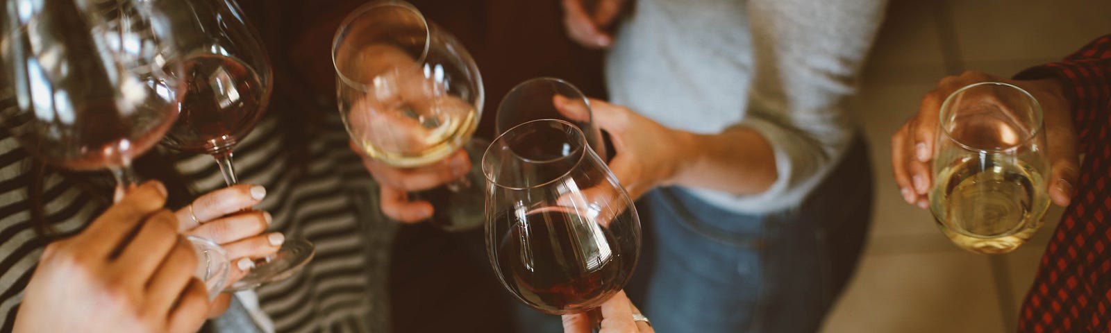 Several hands raise glasses of white wine, with the image from taken from above. A new study suggests that one or two drinks daily are not better than abstaining