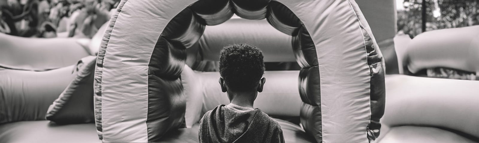 A gray image of a kid looking at a bouncy house away from the camera.