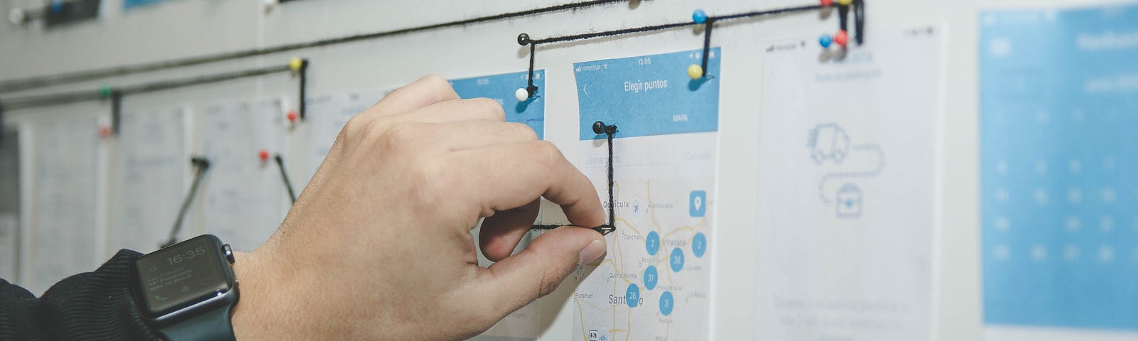 Paper screen mockups on a wall connected by bits of yarn to convey user experience flow
