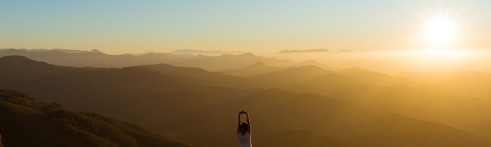 Woman doing yoga tree pose on mountaintop with sunrise