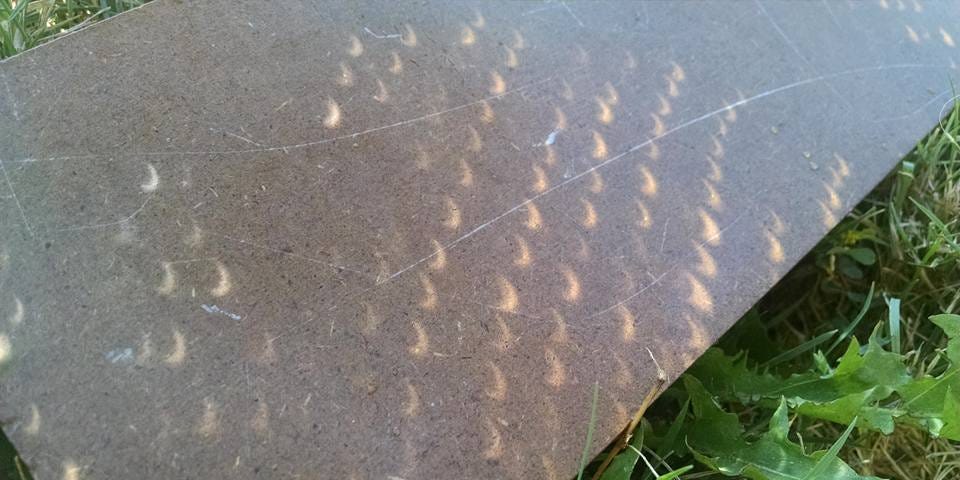 Sidewalk with shadows of partial eclipse filtered through tree leaves.