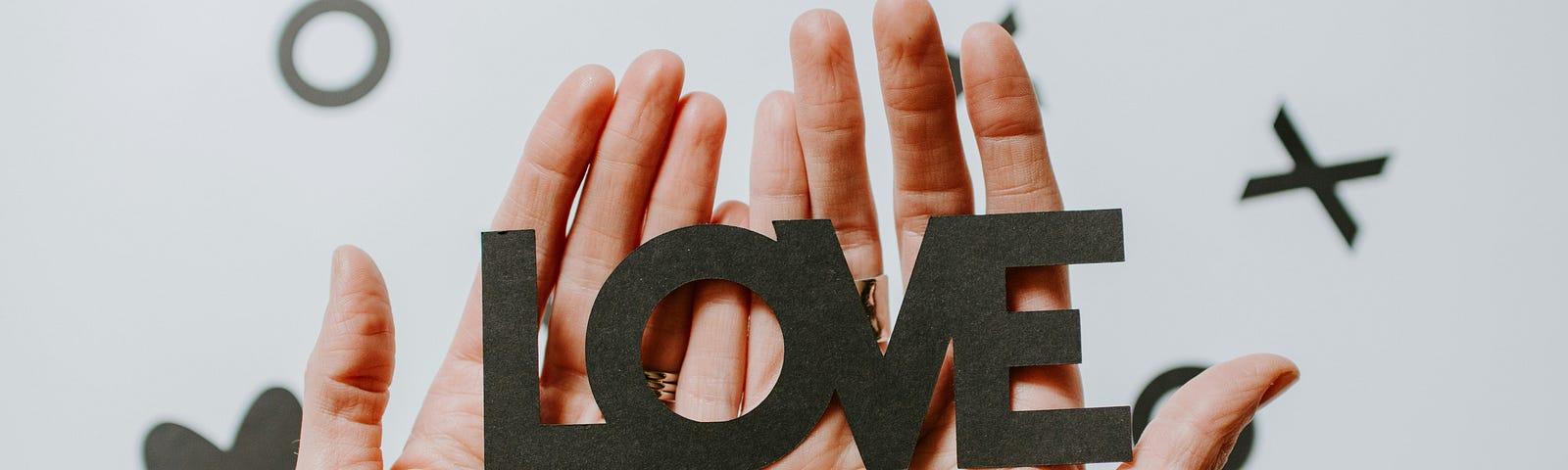 Cutout letters spelling love, held together with two hands.