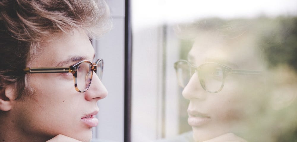Young Man With Glasses Staring Out A Window