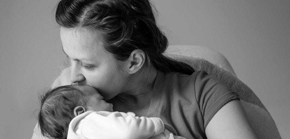 Woman holding baby close, her mouth near baby’s forehead.