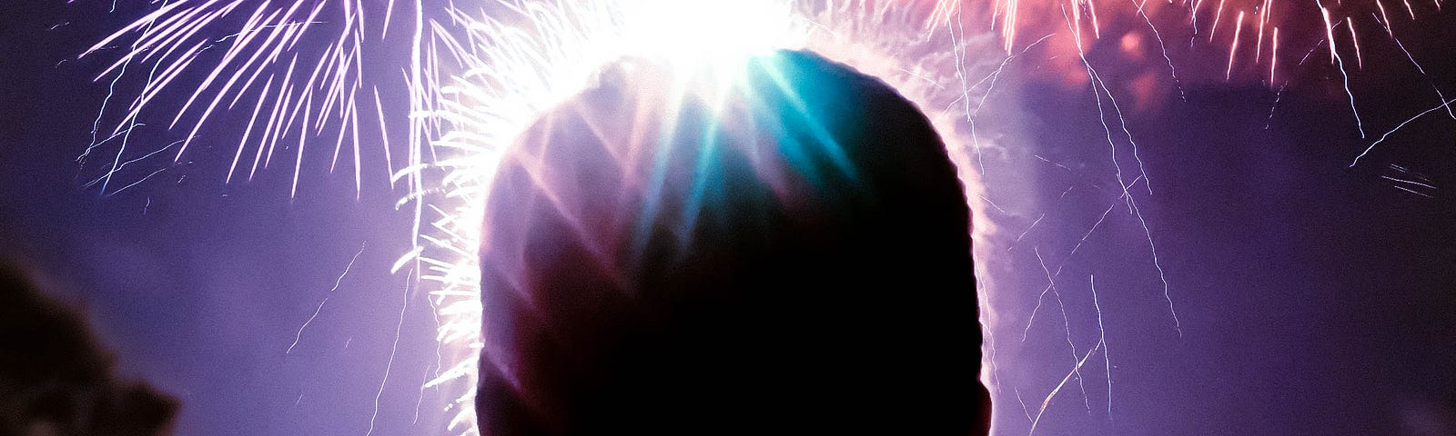 A silhouette of a person’s head against a sky of exploding fireworks