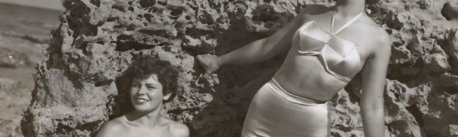 Three beautiful ladies posing in their swimsuits against a rock by the sea. It must be in the 50’s