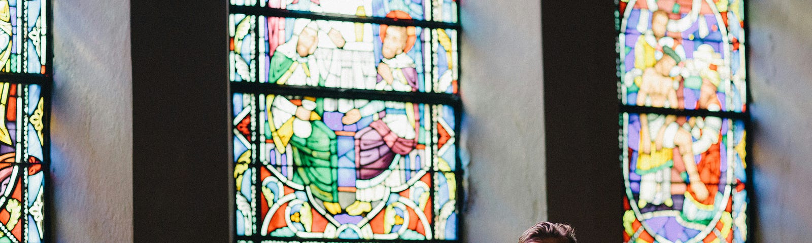 A man sitting in a church with stained glass windows behind him