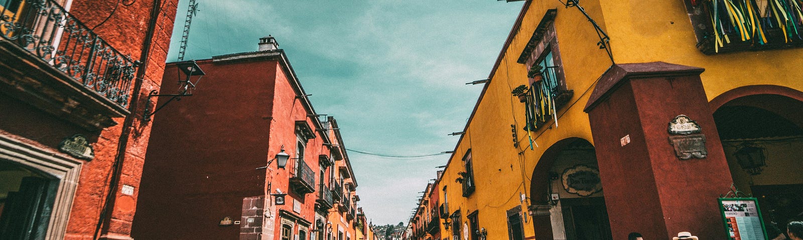 A view of a street in Mexico reminiscent of Mexico City’s Coyoacan neighborhood, featuring colonial buildings and brightly colored folkloric items.