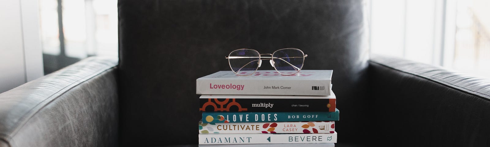A pile of books and reading glasses placed on a sofa.