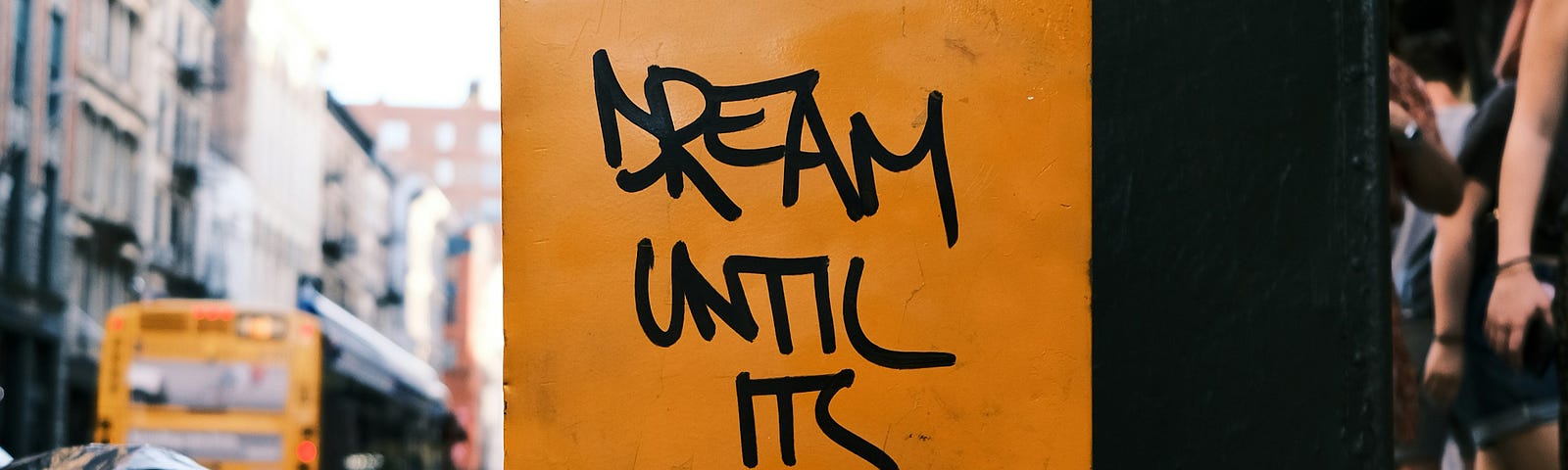graffiti on a yellow newspaper stand in the city (DREAM UNTIL ITS YOUR OWN REALITY)