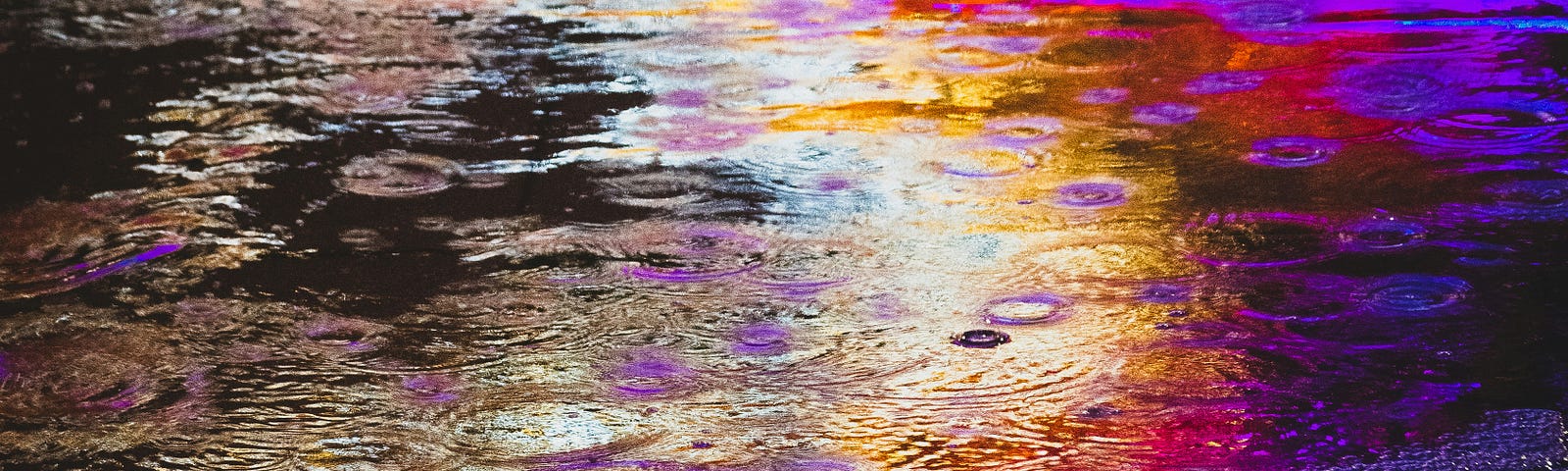 a puddle that is a bit grainy looking with a dim spectrum of colour: purple, pink, red, orange, yellow, and white