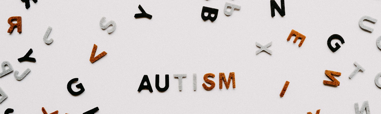 A collection of scrambled letters is laid out across the table. A small group of them in the center are lined up, spelling the word ‘autism’ in blue, white and orange.