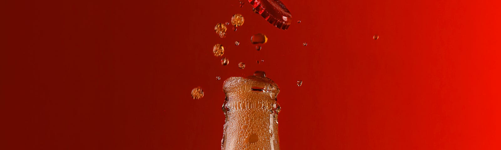 A Coke bottle fizzes and pops it’s lid in front of a plain red background.