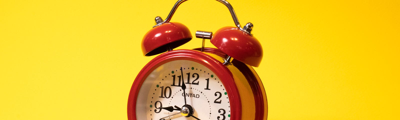 Bright red old-fashioned alarm clock set against a bright yellow background.