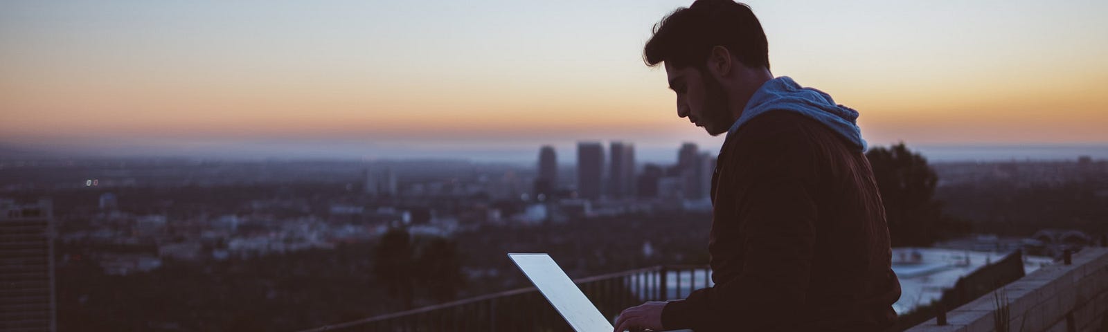 A man works at a laptop while sitting on a rooftop