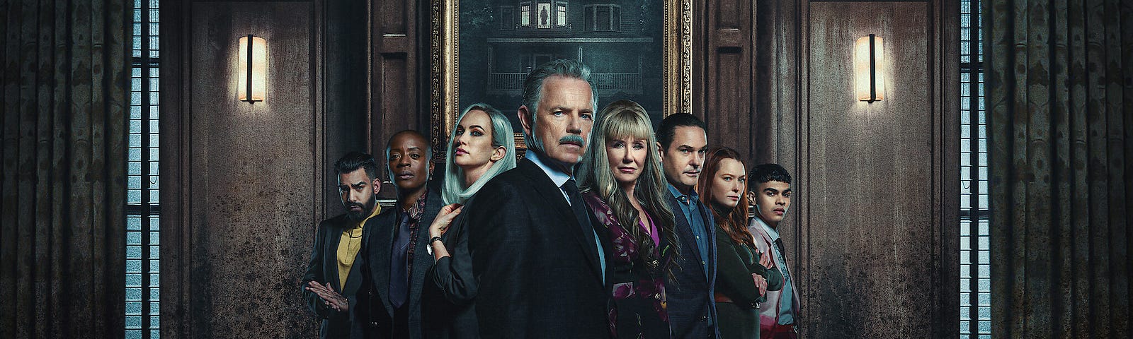 An image shows the main cast of The Fall of the House of Usher standing in a triangle formation. From far left to far right are Rahul Kohli, T’Nia Miller, Kate Siegal, Bruce Greenwood, Mary McDonnell, Henry Thomas, Samantha Sloyan, and Sautiyan Sapkota. The cast stands in a sombre room with the portrait of an old bungalow behind them.