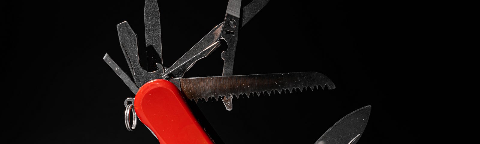 Photo of red pocket knife multi-tool propped up at a 45˚ angle, with all its tools extended at different angles