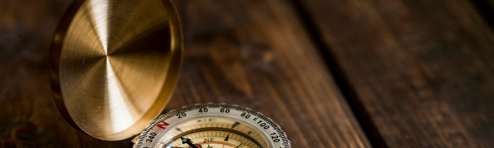 A gold-cased compass, open on a wooden plank table.