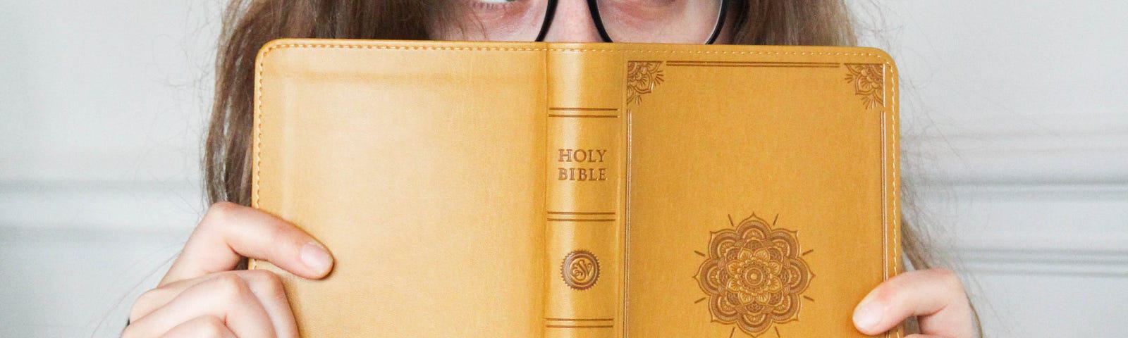 A young woman peers at something from behind a Bible.